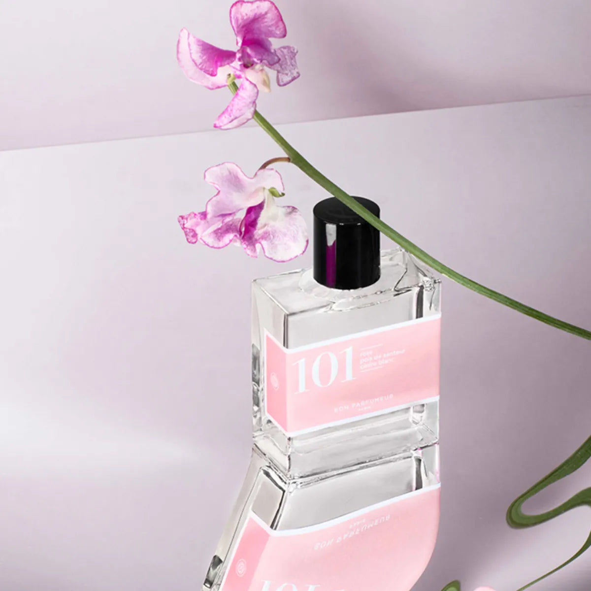 Bon Parfumeur - Les Classiques - 101 Parfumflakon mit zartrosa Etikett und schwarzem Verschluss vor hellem Hintergrund mit blühender Blume
