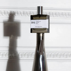 Bon Parfumeur - Les Privés - 104 Parfumflakon mit rauchigem Glas und weißem Etikett vor hell strukturiertem Hintergrund