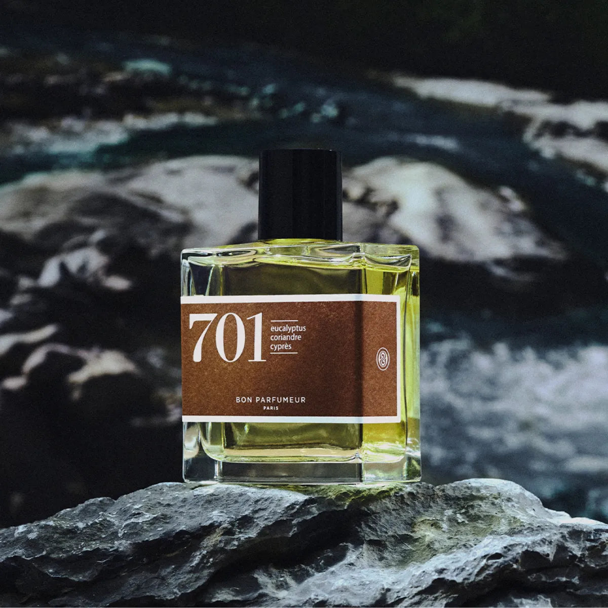 Bon Parfumeur - Les Classiques - 701 Parfumflakon mit braunem Etikett auf Felsen vor düsterer Flusslandschaft