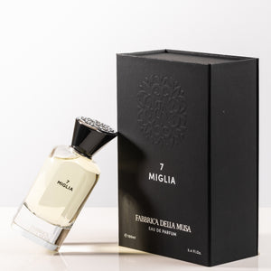 Fabbrica della Musa - 7 Miglia klarer Flakon mit schwarzem, verziertem Verschluss neben schwarzer edler Verpackung