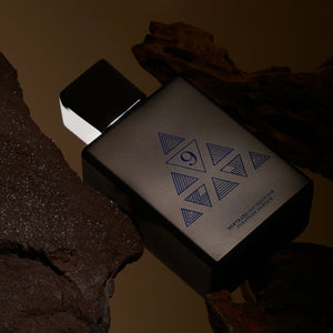 Spiritum - 9 - Final Spirit Parfumflakon mit mattschwarzem Design und geometrischem Muster auf dunklem Untergrund aus Holz und Stein