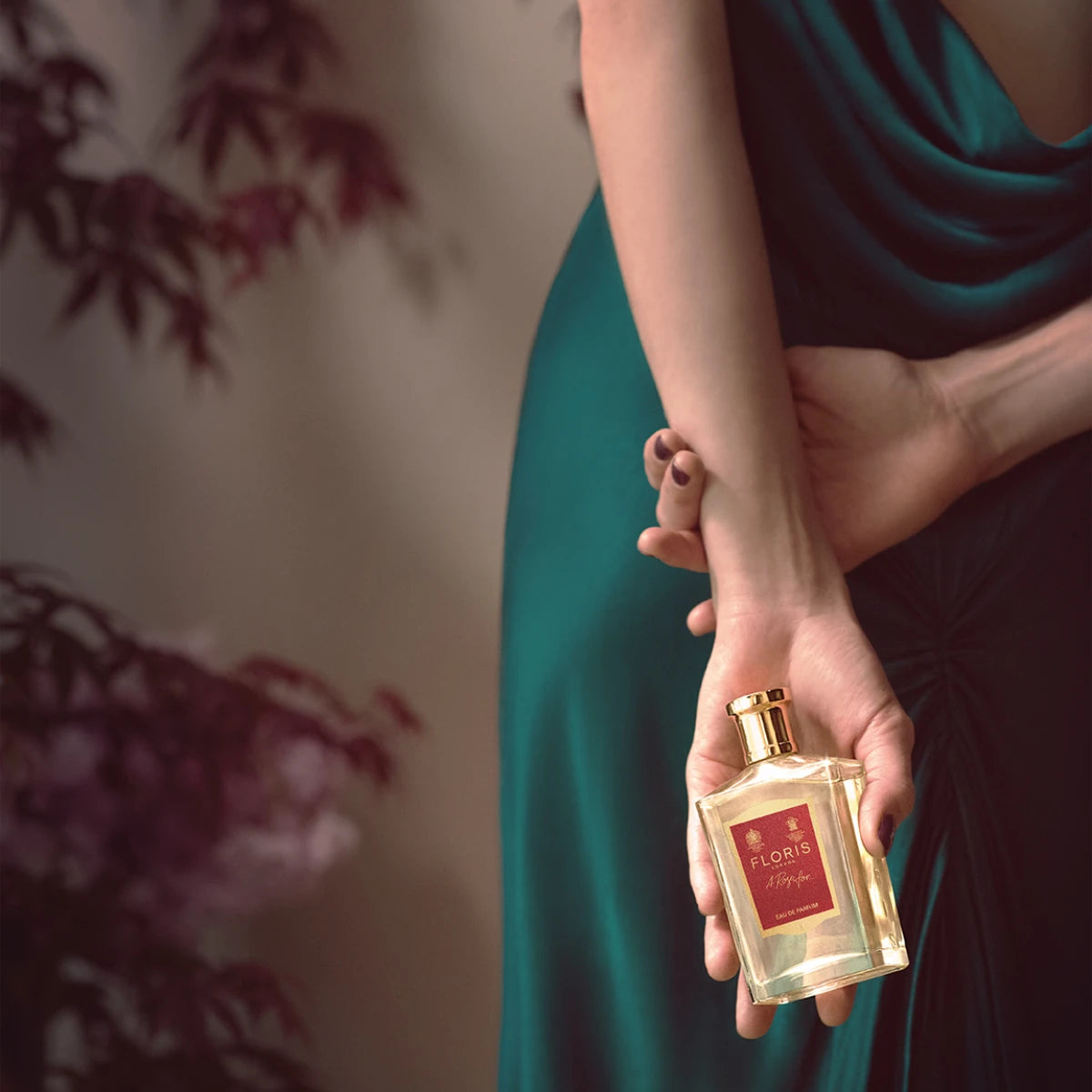 Floris - A Rose for... Parfümflakon mit goldenem Verschluss in eleganter Hand vor grünem Kleid und Pflanzenhintergrund