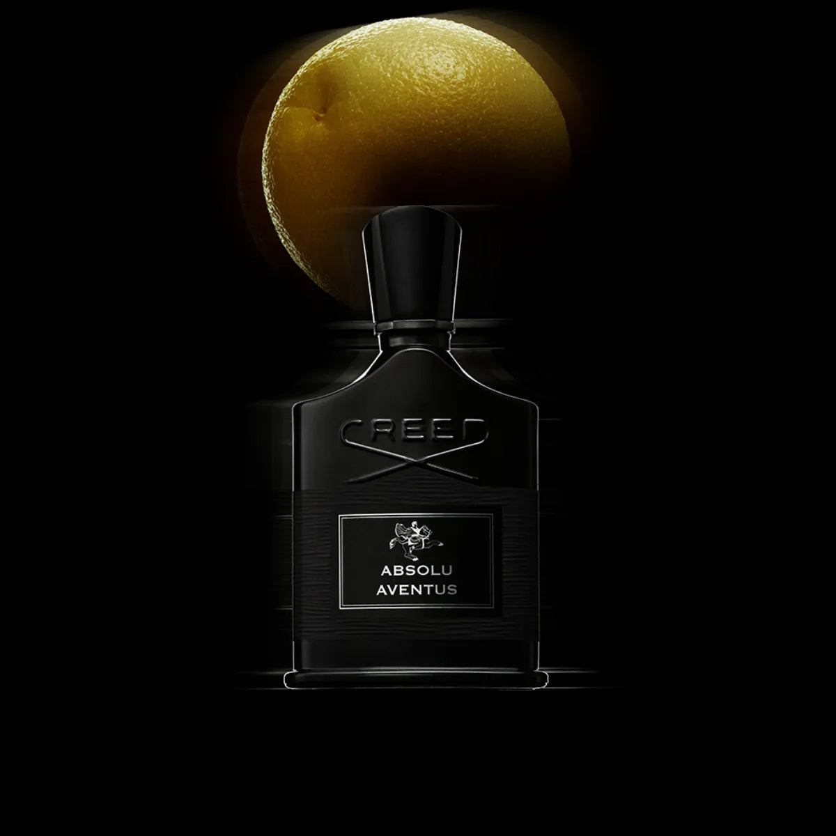 Creed - Absolu Aventus Parfumflakon in tiefem Schwarz mit markanter Prägung und beleuchtet von Zitrusfrucht im Hintergrund