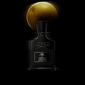Creed - Absolu Aventus Parfumflakon in tiefem Schwarz mit markanter Prägung und beleuchtet von Zitrusfrucht im Hintergrund