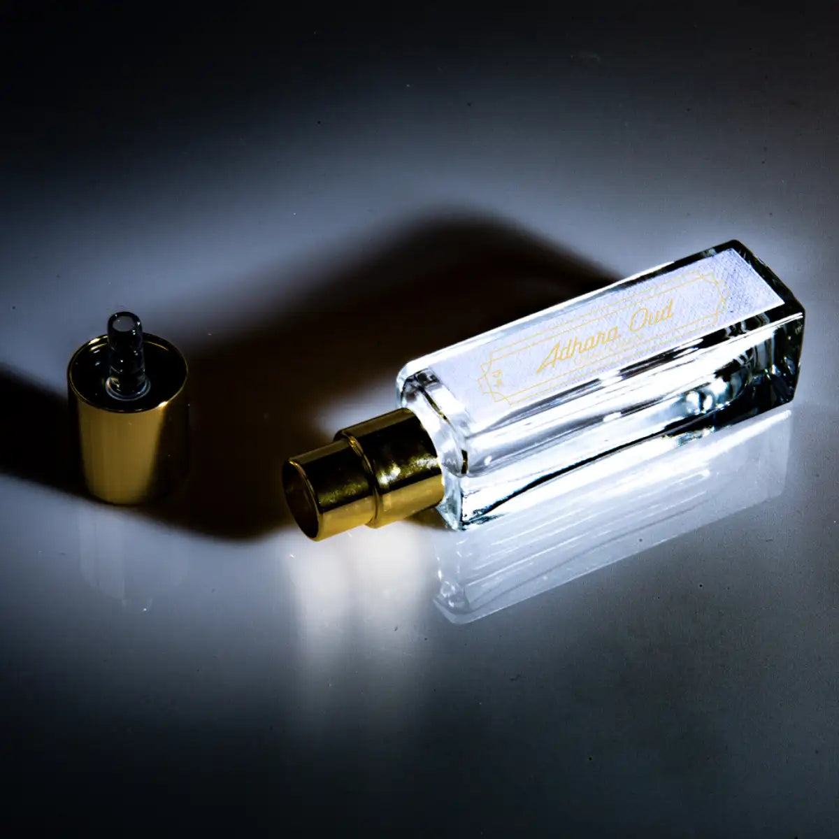 Cherigan - Adhara Oud Parfumflakon mit goldenem Zerstäuber und transparentem Glas auf reflektierender Oberfläche