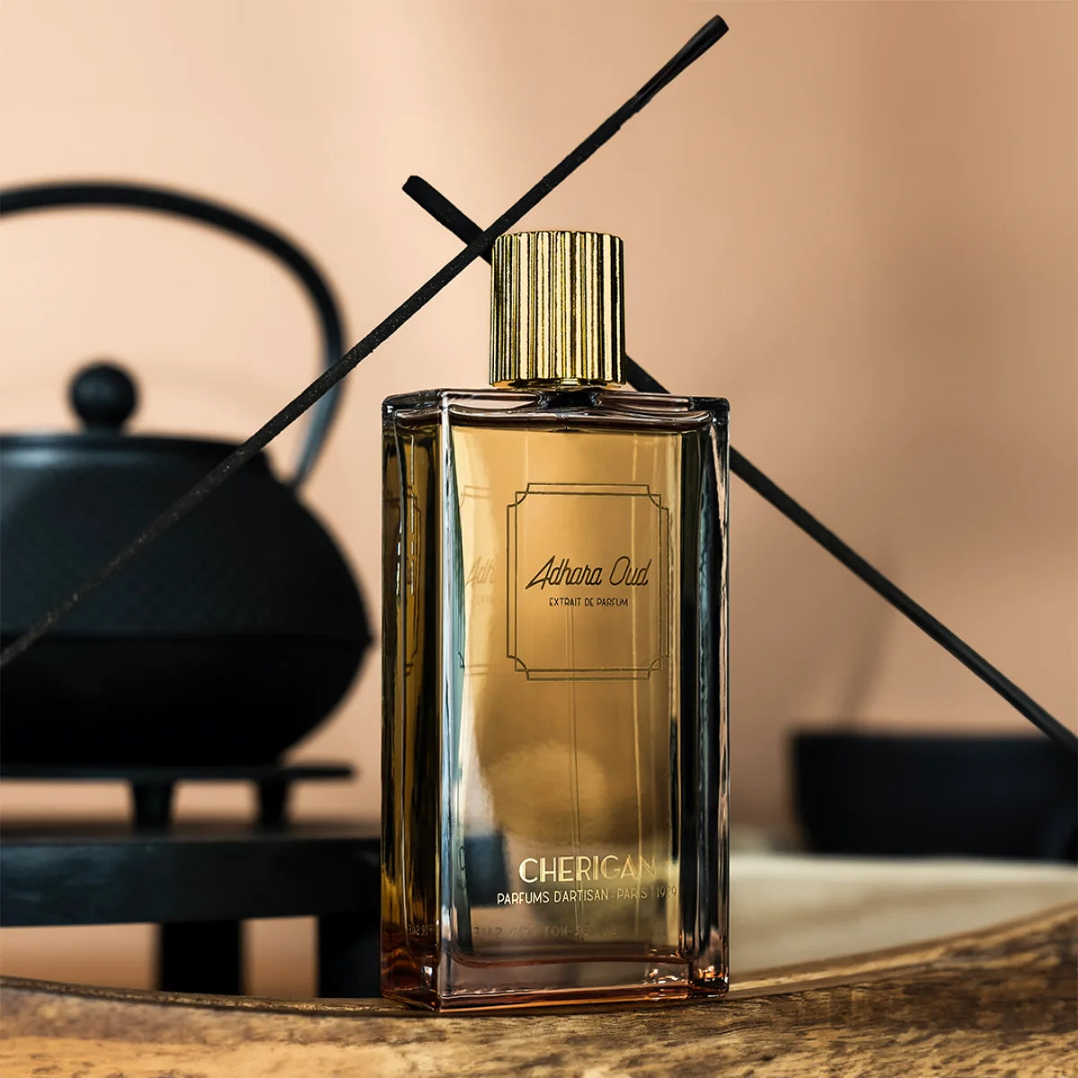 Cherigan - Adhara Oud Parfumflakon mit goldenem Verschluss auf Holztisch vor asiatischem Teekessel und Hintergrund