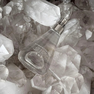 Nomenclature - adr_ett Sprayflakon mit transparentem Glas und silbernem Zerstäuber auf Kristallsteinen liegend