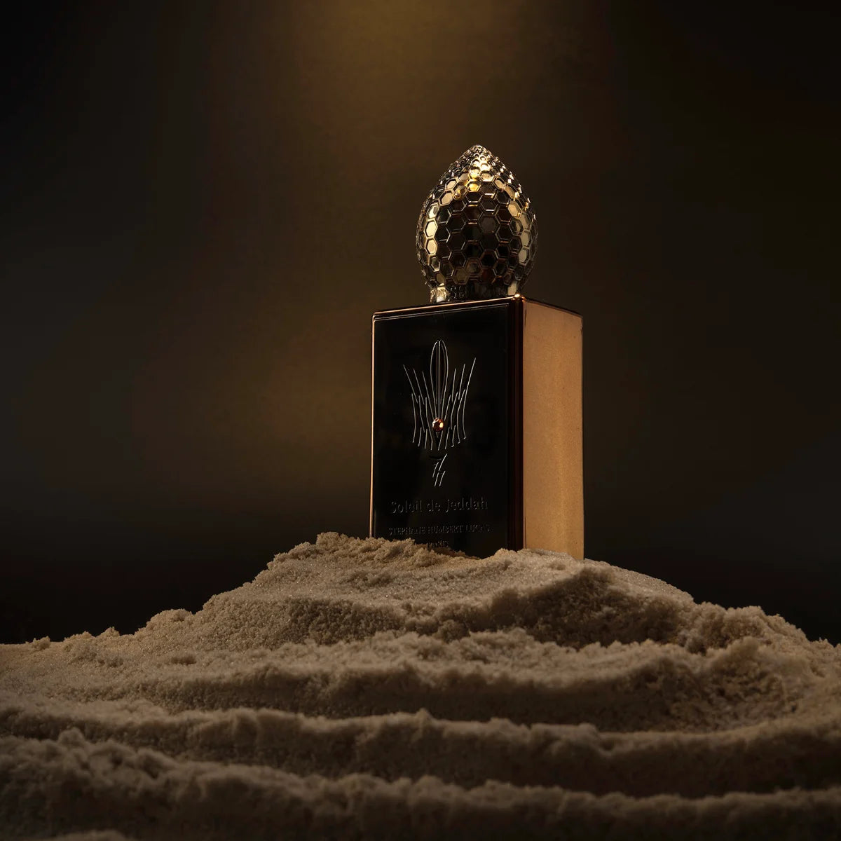 Stéphane Humbert Lucas 777 - Afterglow Flakon mit honigwabenartigem Deckel auf sandiger Oberfläche vor dunklem Hintergrund