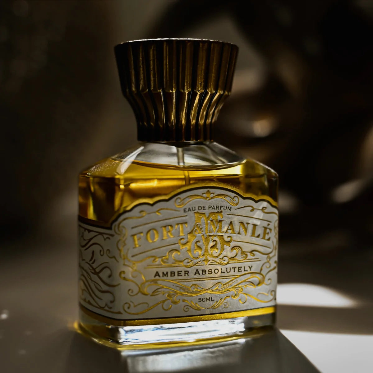 Fort & Manlé - Amber Absolutely Parfüm mit goldenem, verzierter Flakon und zeitlos elegantem Verschluss im warmen Licht