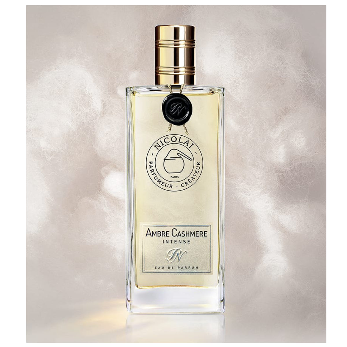 Nicolaï - Ambre Cashmere Intense Parfumflakon mit goldenem Verschluss vor cremigem, weich wirkendem Hintergrund