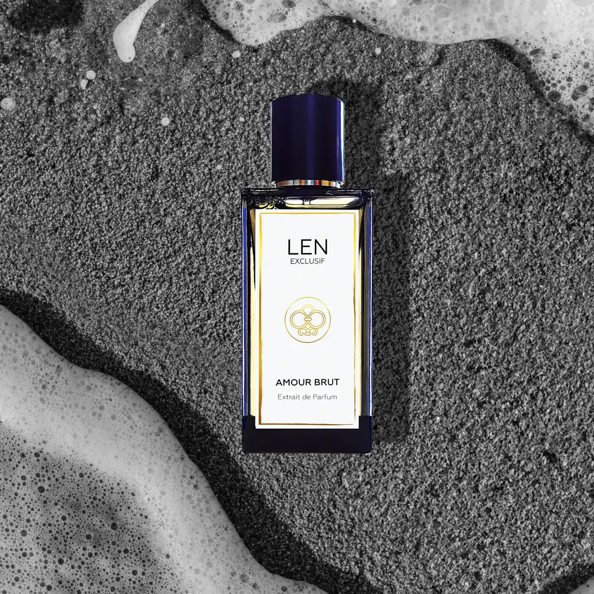 LEN - Amour Brut Parfumflakon mit blauem Deckel und elegantem, klaren Design auf sandigem Untergrund mit Meeresrauschen
