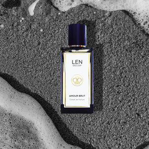 LEN - Amour Brut Parfumflakon mit blauem Deckel und elegantem, klaren Design auf sandigem Untergrund mit Meeresrauschen