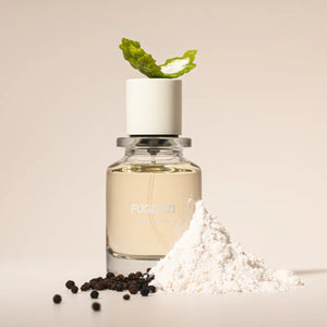 Fugazzi - Angel Dust Parfumflakon mit klarem Duft, weißem Verschluss, umgeben von Pulver und Pfefferkörnern vor hellem Hintergrund