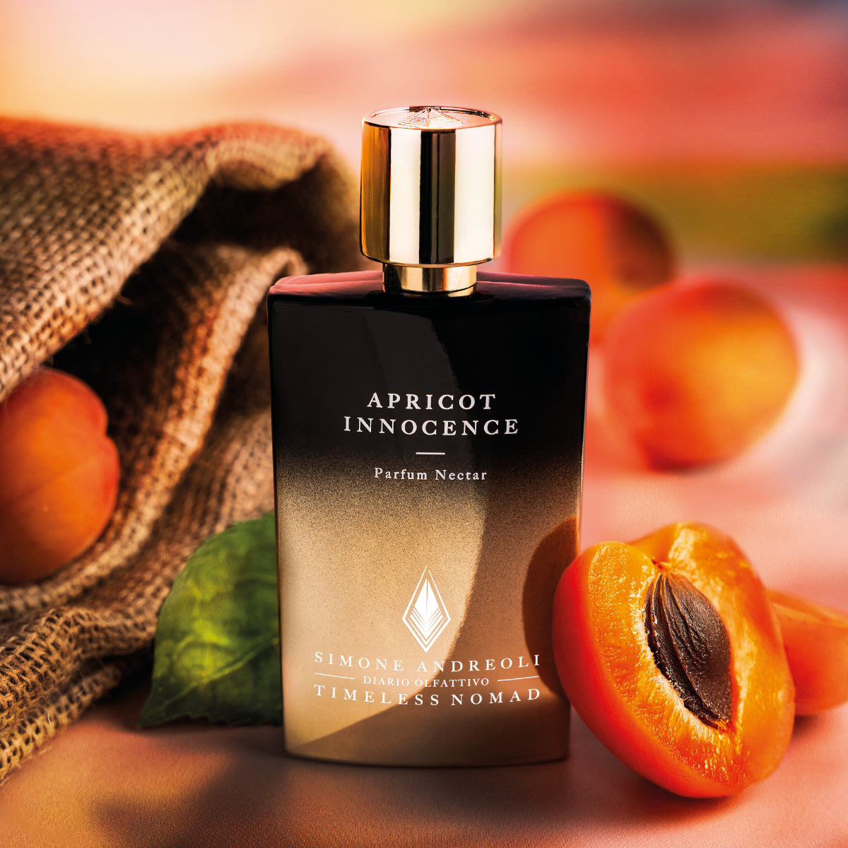 Simone Andreoli - Apricot Innocence Parfumflakon mit gold schwarzem Deckel neben frischen Aprikosen und Jutesack