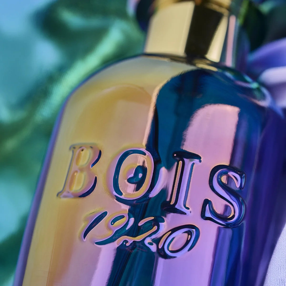 Bois 1920 - Trasparenti - Art1920 Flakon mit irisierendem Glas und goldfarbenem Verschluss in Nahaufnahme vor buntem Hintergrund