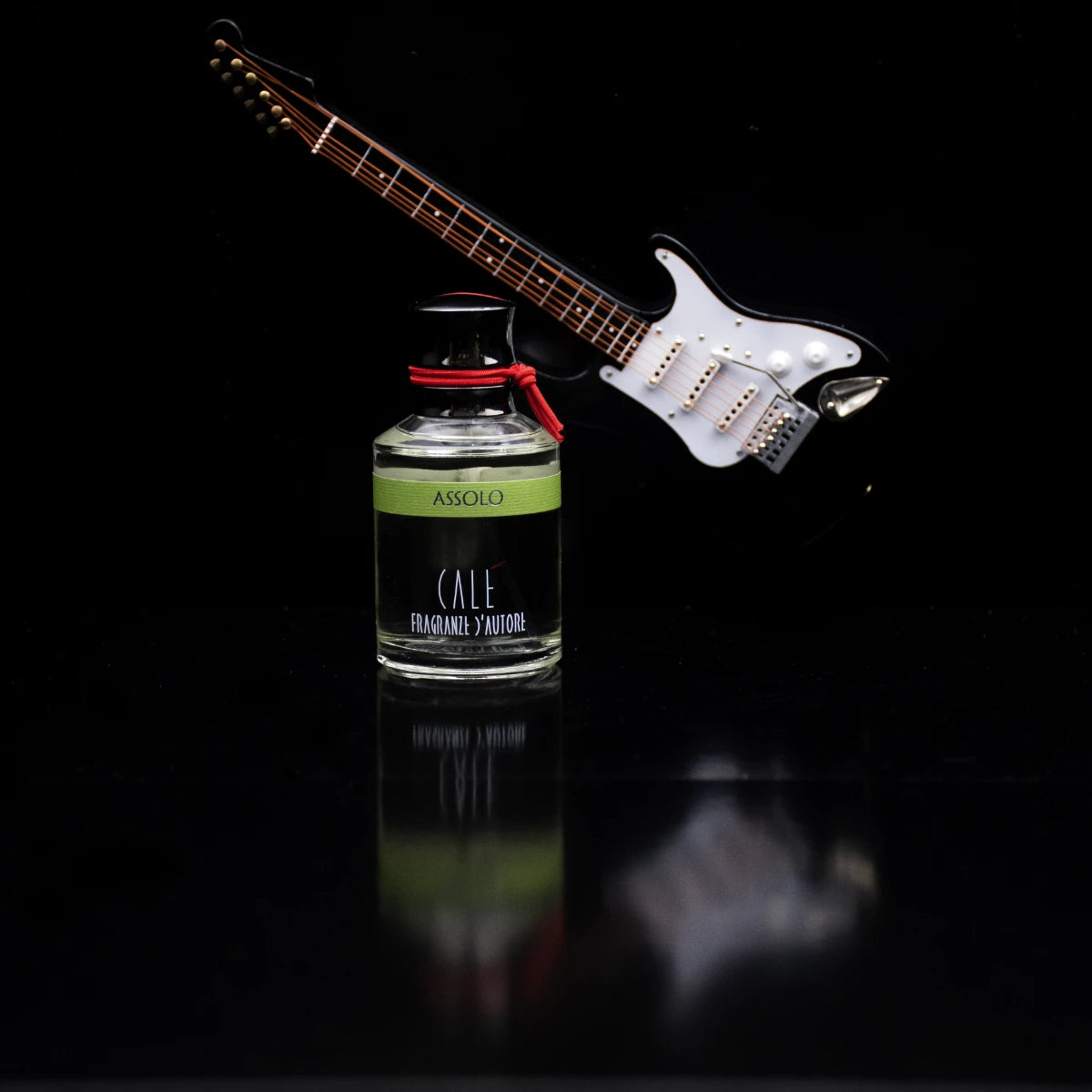 Calé Fragranze d'Autore - Assolo Duftflakon mit rotem Band vor elektrischem Gitarrenmodell auf schwarzem Hintergrund