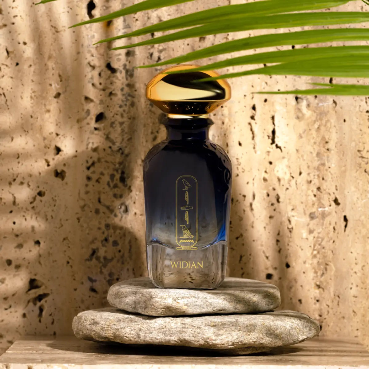 Widian - Sapphire Collection - Aswan Parfumflakon in dunkelblauem Glas mit goldenem Verschluss auf Natursteinen vor texturierter Wand