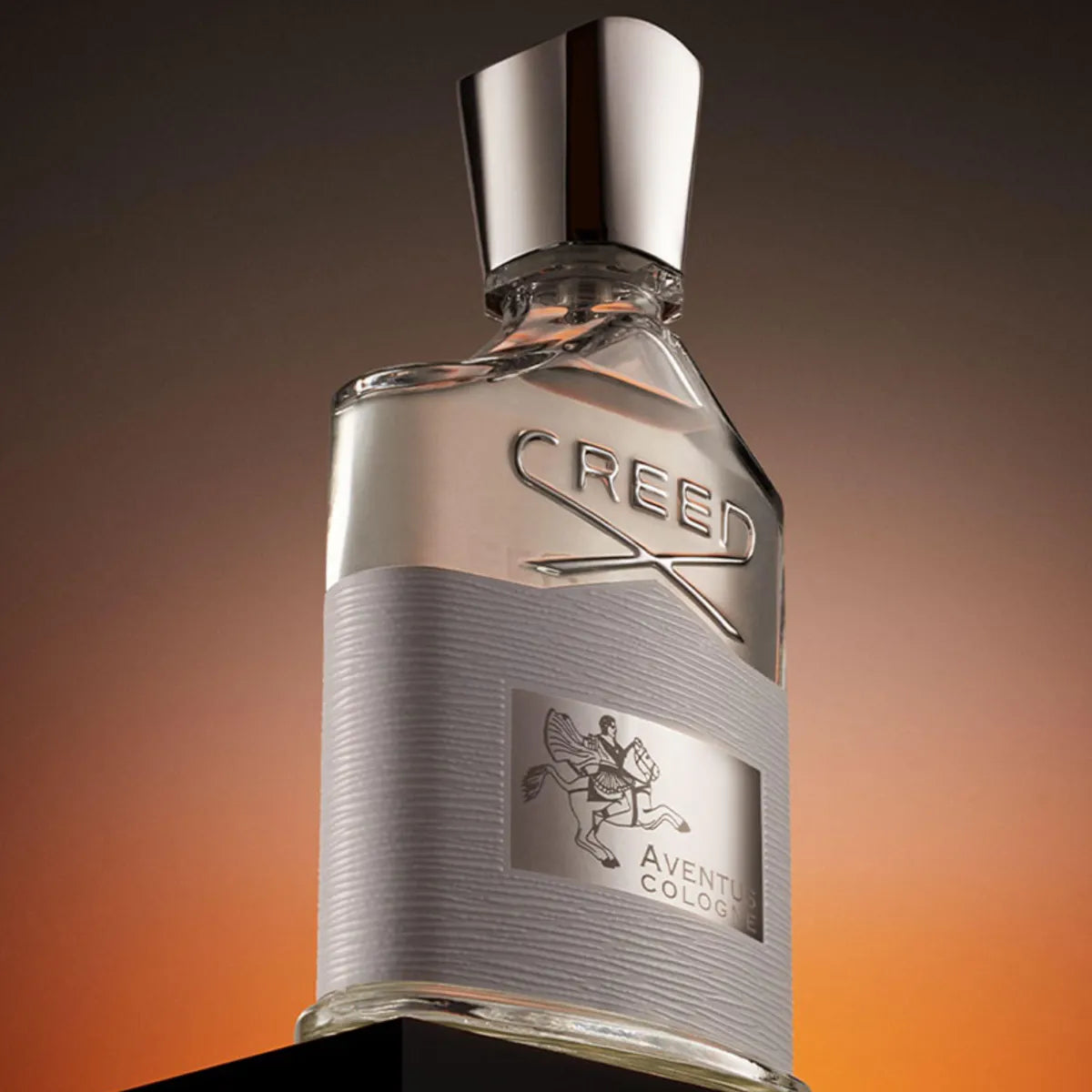 Creed - Aventus Cologne Flakon mit schimmerndem silbernem Verschluss und dezenter Prägung vor warmem Hintergrund