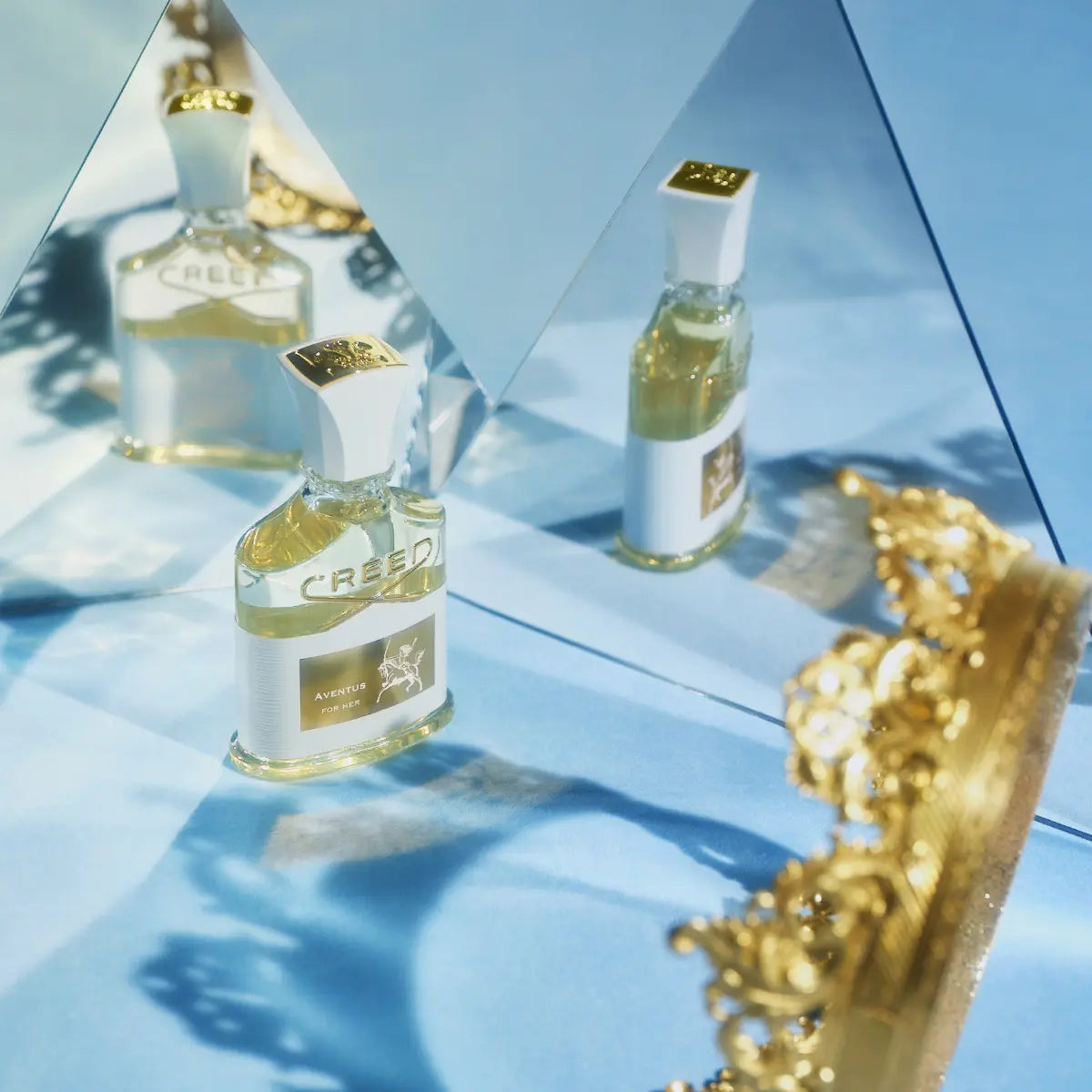Creed - Aventus for Her Flakon mit weißem Verschluss und goldenem Label vor Spiegelreflexion auf blauem Hintergrund