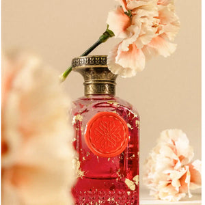 Anfas - Fosol Collection - Aya Parfumflakon mit rotem Siegel und goldenen Details umgeben von zarten Blütenblättern