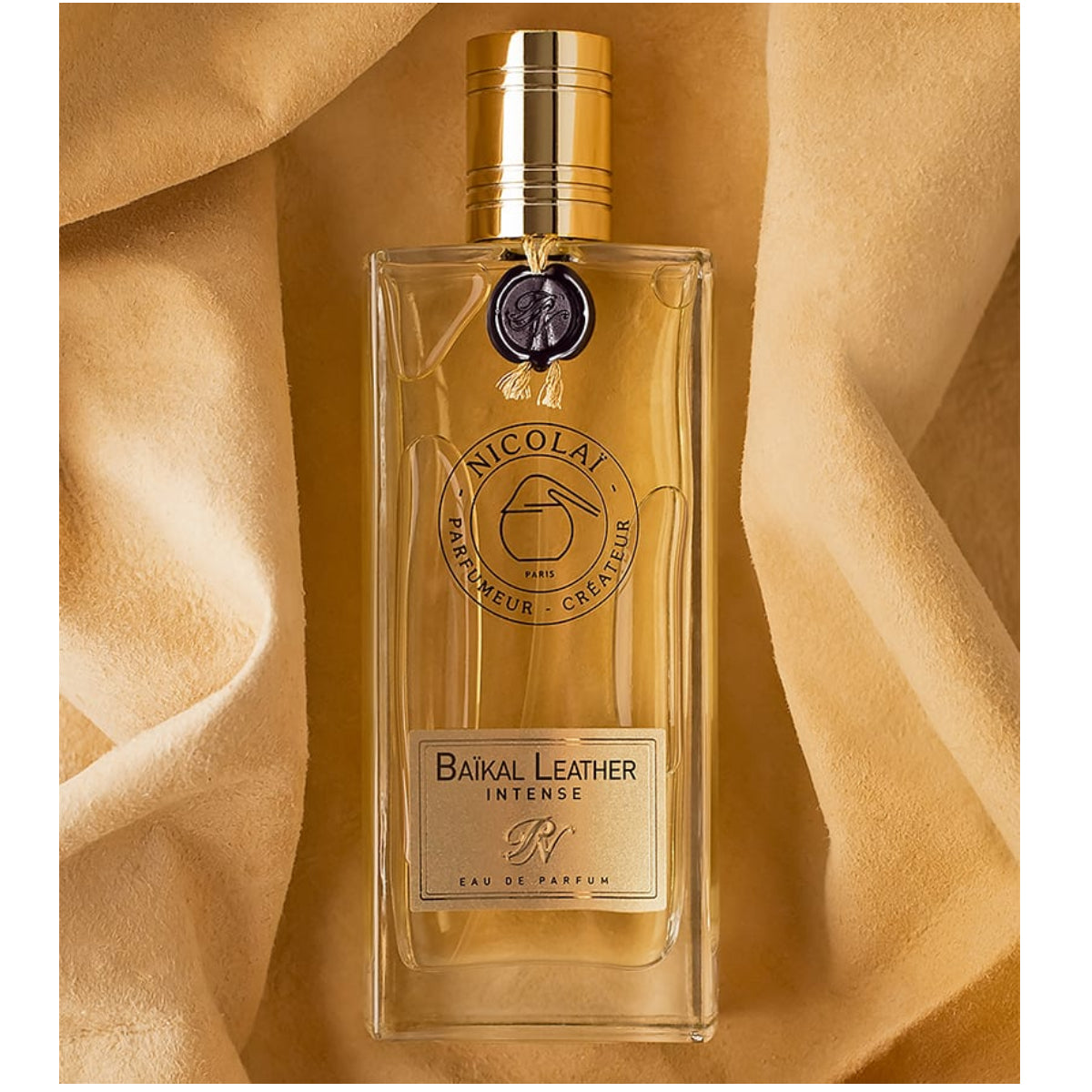 Nicolaï - Baïkal Leather Intense Parfumflakon mit goldenem Verschluss auf samtigem beigem Hintergrund