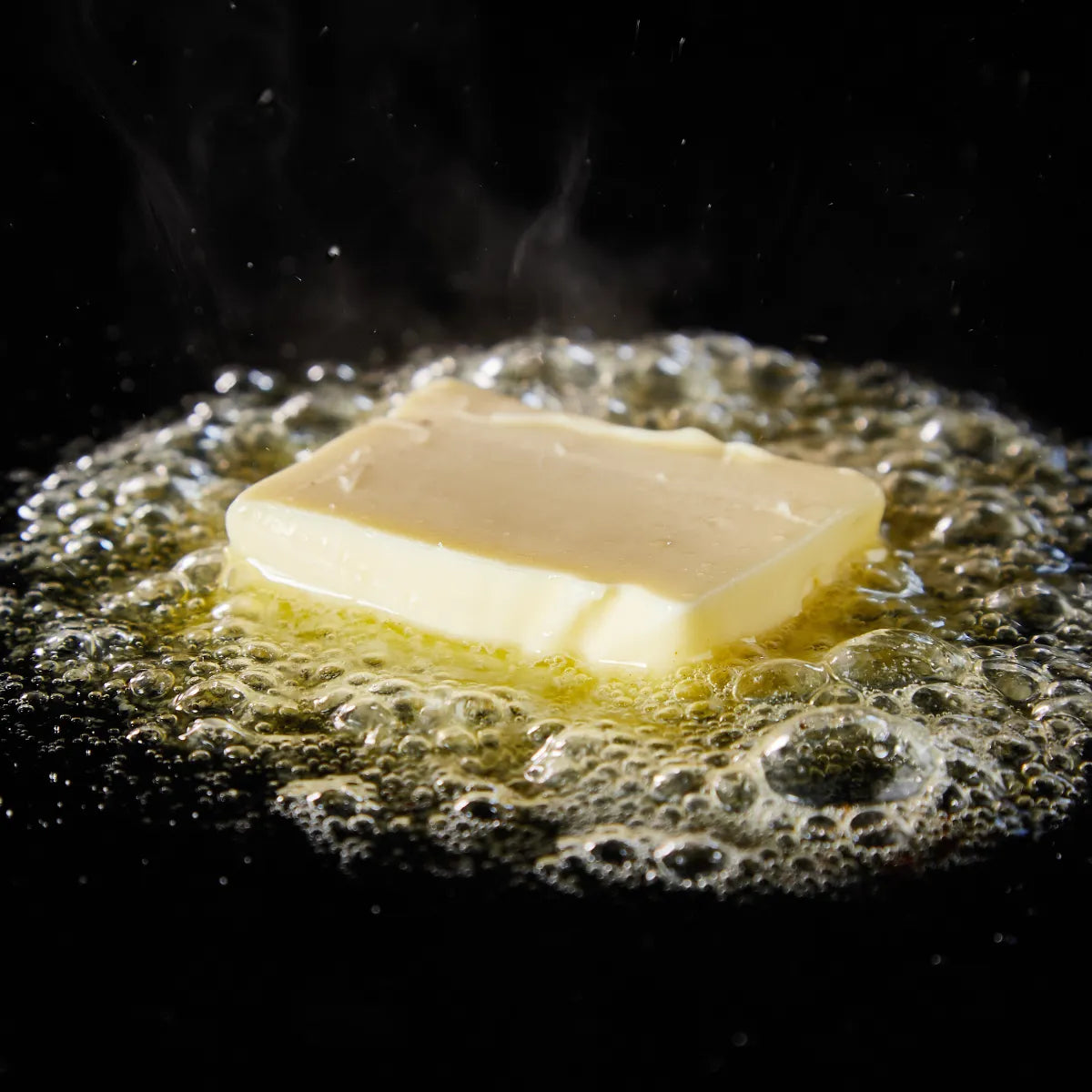 Sensatio Paris - Beurre de Santal zerlaufende Butter in Pfanne auf dunklem Hintergrund mit aufsteigendem Dampf