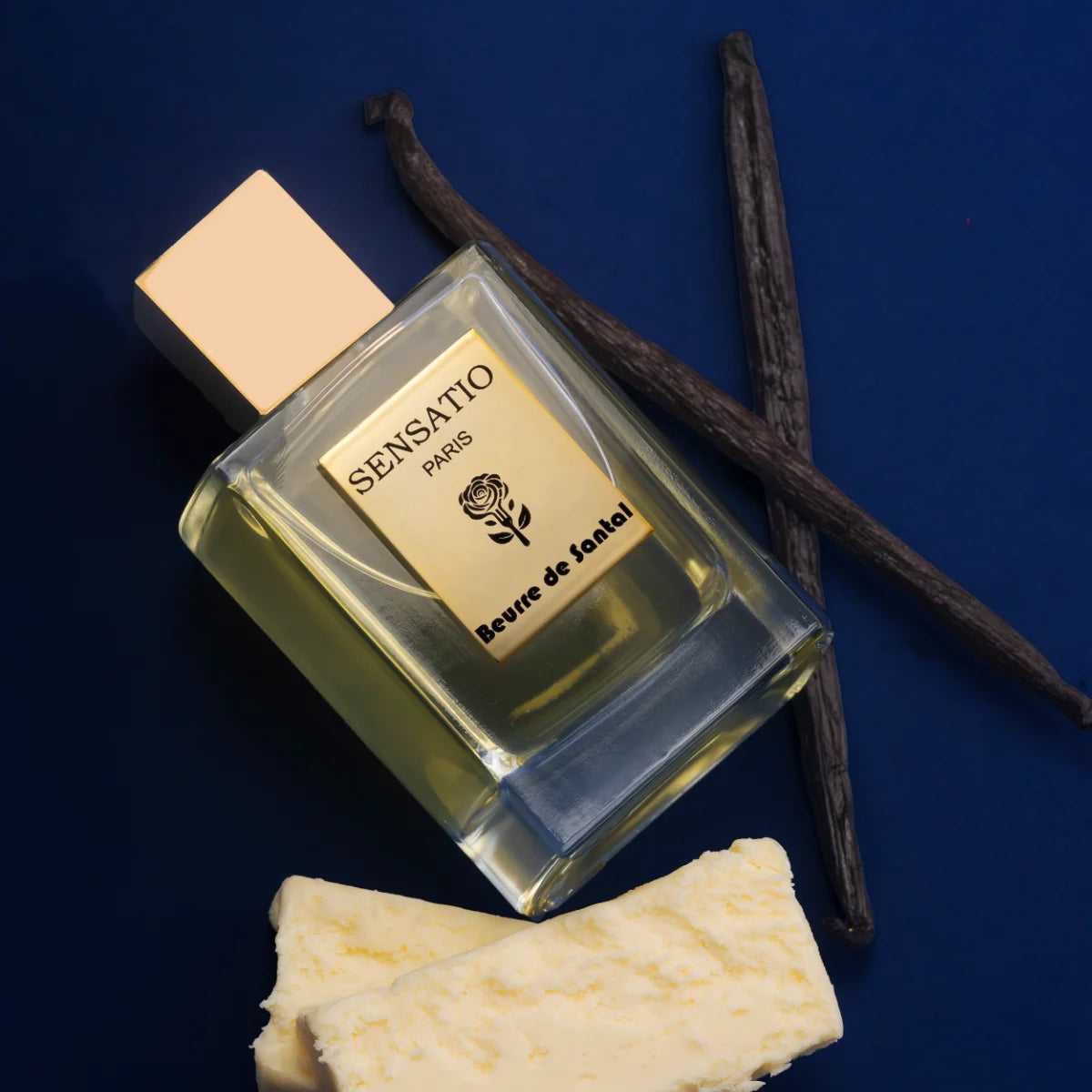 Sensatio Paris - Beurre de Santal Parfumflakon mit goldfarbenem Verschluss, Bourbon-Vanilleschoten und Butterstücken auf dunklem Hintergrund