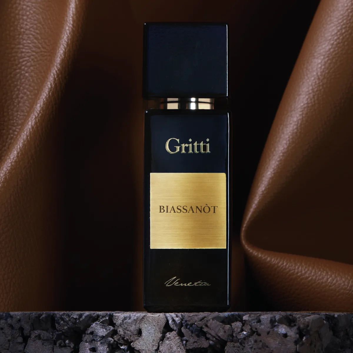 Gritti - Black Collection - Biassanòt Parfumflakon in tiefschwarzem Design mit goldenem Etikett vor braunem Lederhintergrund