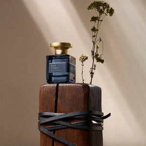 Atelier Materi - Black Oregano zeigt dunkelblauen Flakon mit goldenem Verschluss auf Holzsockel und getrocknetem Zweig