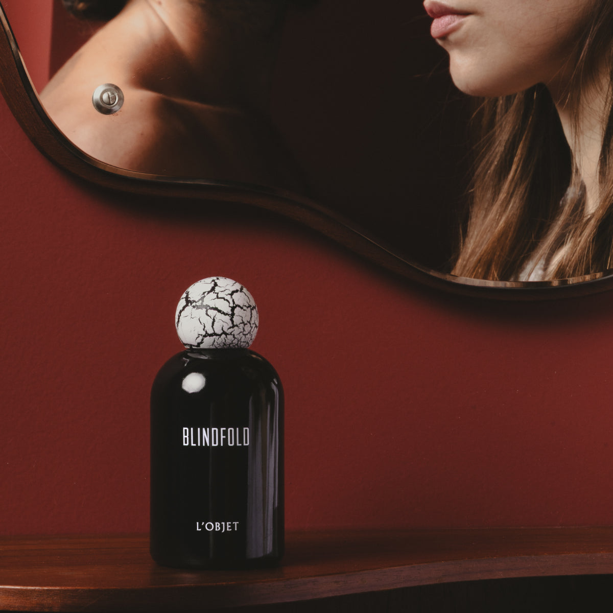 L'Objet - Blindfold Eau de Parfum mit elegantem schwarzen Flakon und kunstvoll marmoriertem Verschluss vor rotem Hintergrund