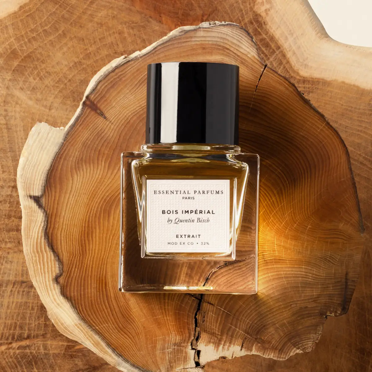 Essential Parfums - Bois Impérial - Extrait de Parfum klarer Flakon mit schwarzem Deckel auf Holzscheibe vor hellem Hintergrund