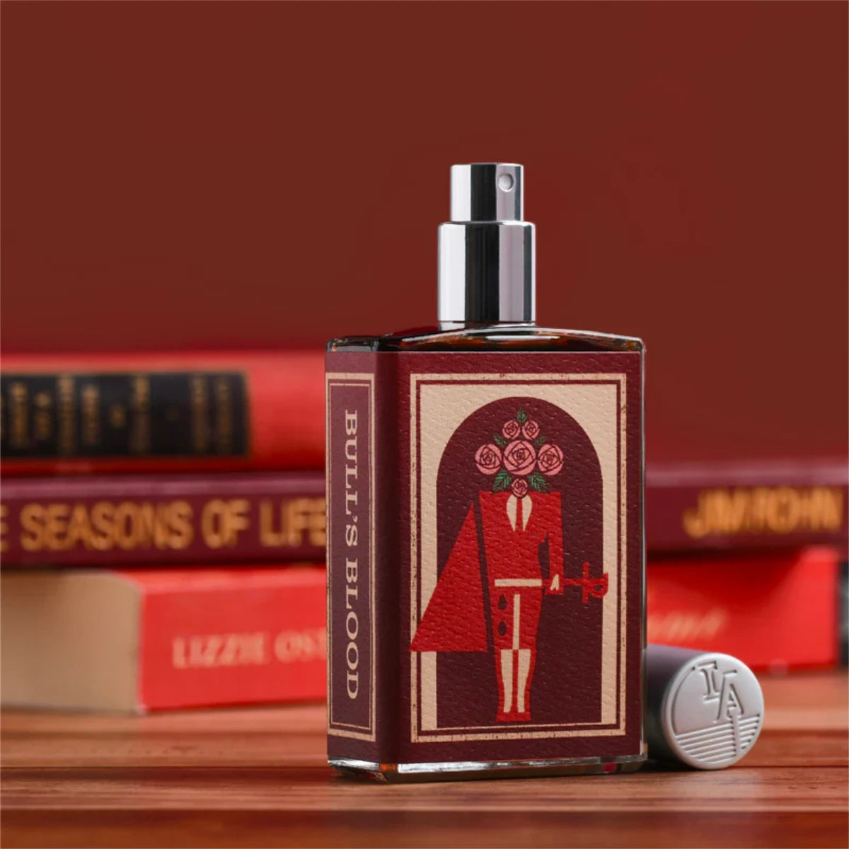 Imaginary Authors - Bull's Blood 2nd Edition Parfumflakon mit rotem Etikett und stilisiertem Figurenmotiv auf Holztisch