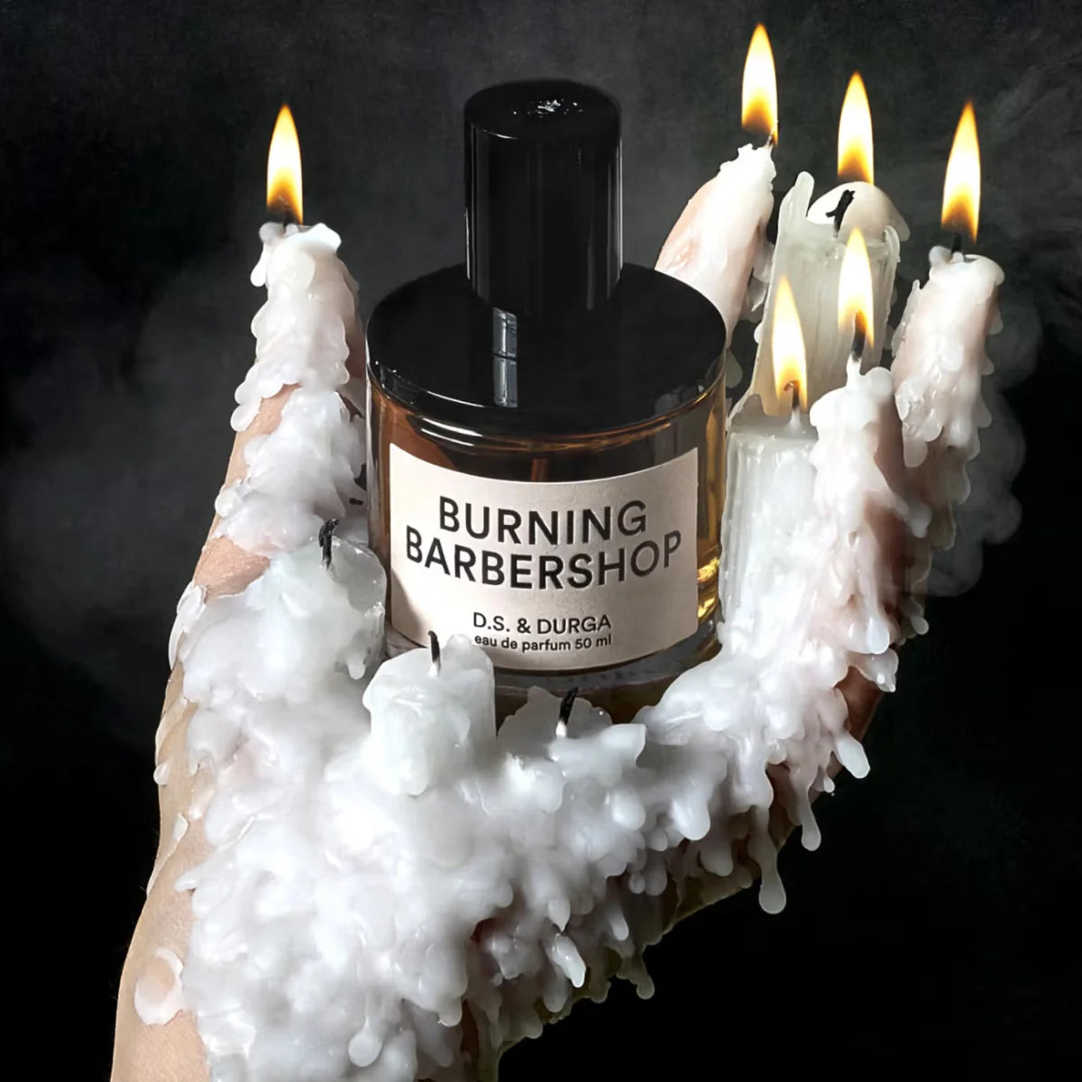 D.S. & Durga - Burning Barbershop Flakon in Hand umhüllt von schmelzendem weißen Wachs mit Flammen vor dunklem Hintergrund