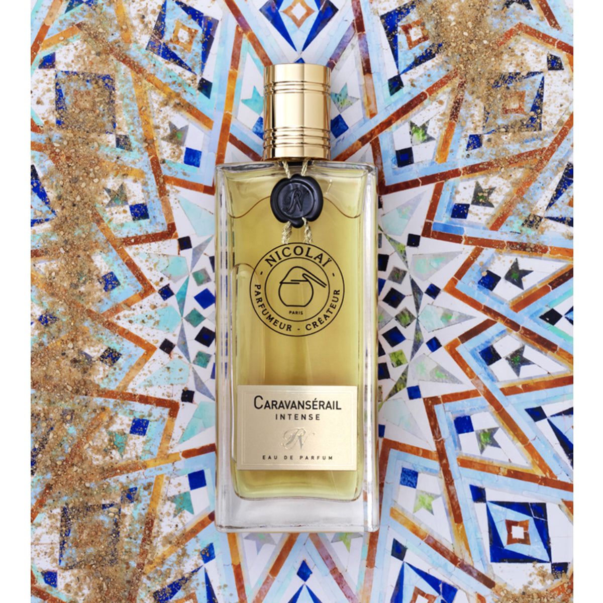 Nicolaï - Caravansérail Intense eleganter Flakon vor farbigem Mosaikhintergrund mit goldfarbenem Verschluss