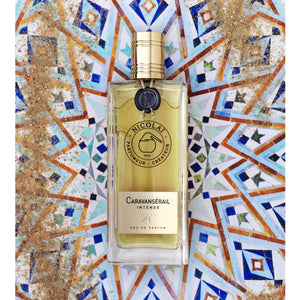 Nicolaï - Caravansérail Intense eleganter Flakon vor farbigem Mosaikhintergrund mit goldfarbenem Verschluss