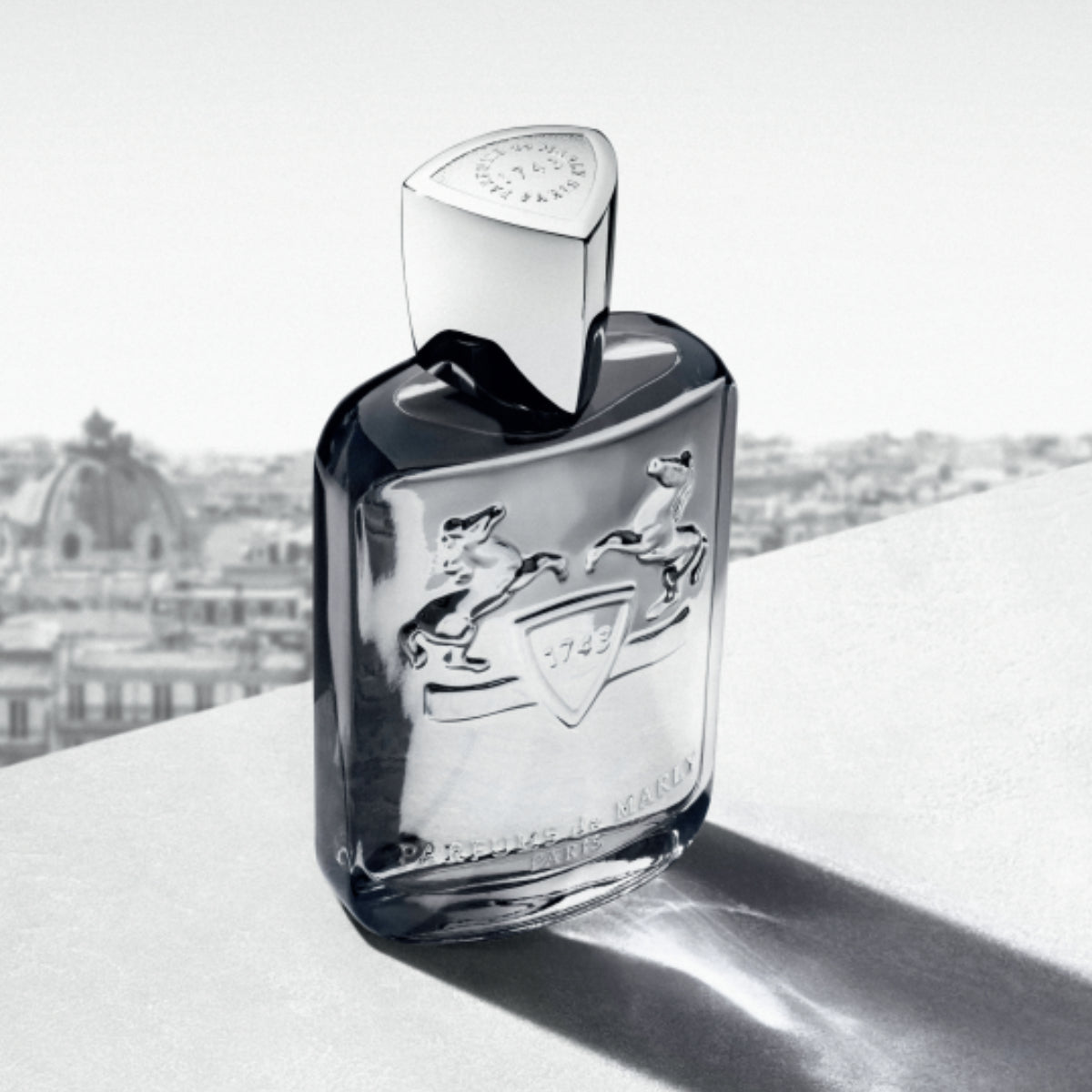 Parfums de Marly - Castley mit silbernem Flakon, geprägtem Wappensymbol und markantem Verschluss vor Stadtpanorama