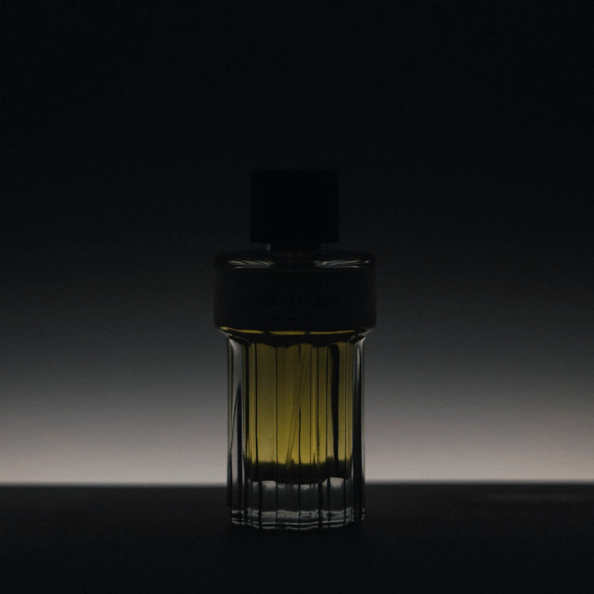 Chambre52 - Contre ta Peau zeigt geheimnisvollen Parfumflakon im dunklen Licht mit strahlendem Gelbton im Glas