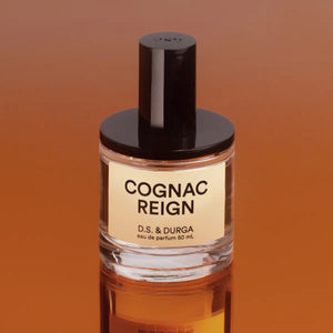 D.S. & Durga - Cognac Reign Parfumflakon mit schwarzem Verschluss vor reflektierendem cognacfarbenem Hintergrund