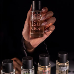 PERFUME.SUCKS - Living Coral 16-1546C Flakon in Hand vor dunklem Hintergrund mit weiteren Parfumflakons im Vordergrund