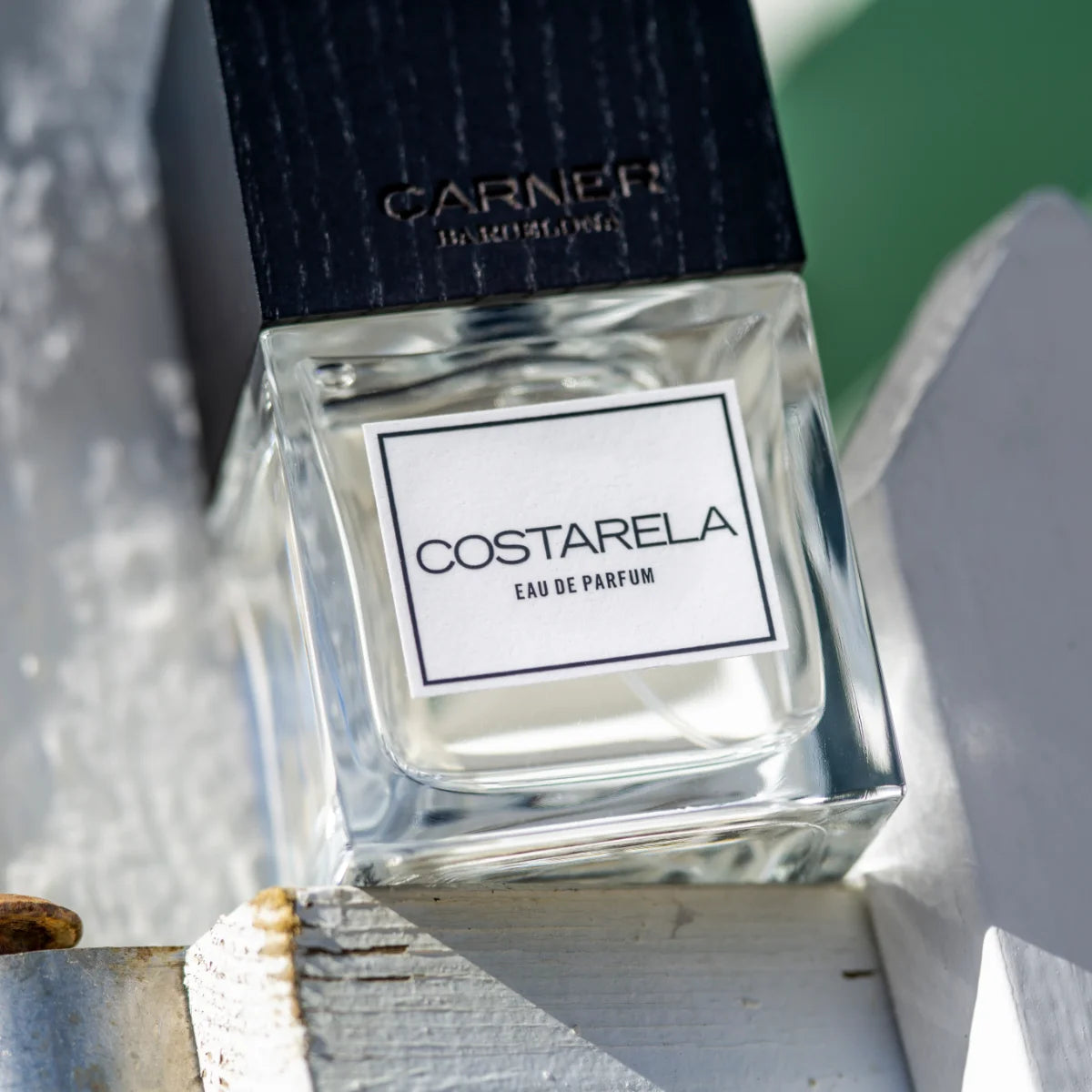 Carner Barcelona - Costarela Parfumflakon mit klarer Flüssigkeit und schwarzem Deckel auf hellem Holzhintergrund