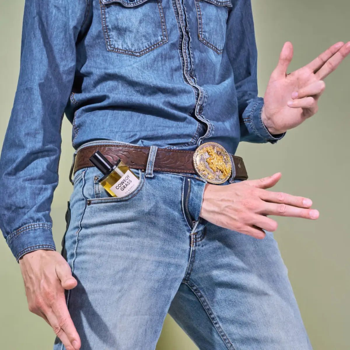 D.S. & Durga - Cowboy Grass Parfümflakon in Jeanshosentasche mit Cowboy-Gürtel und Westernpose vor neutralem Hintergrund
