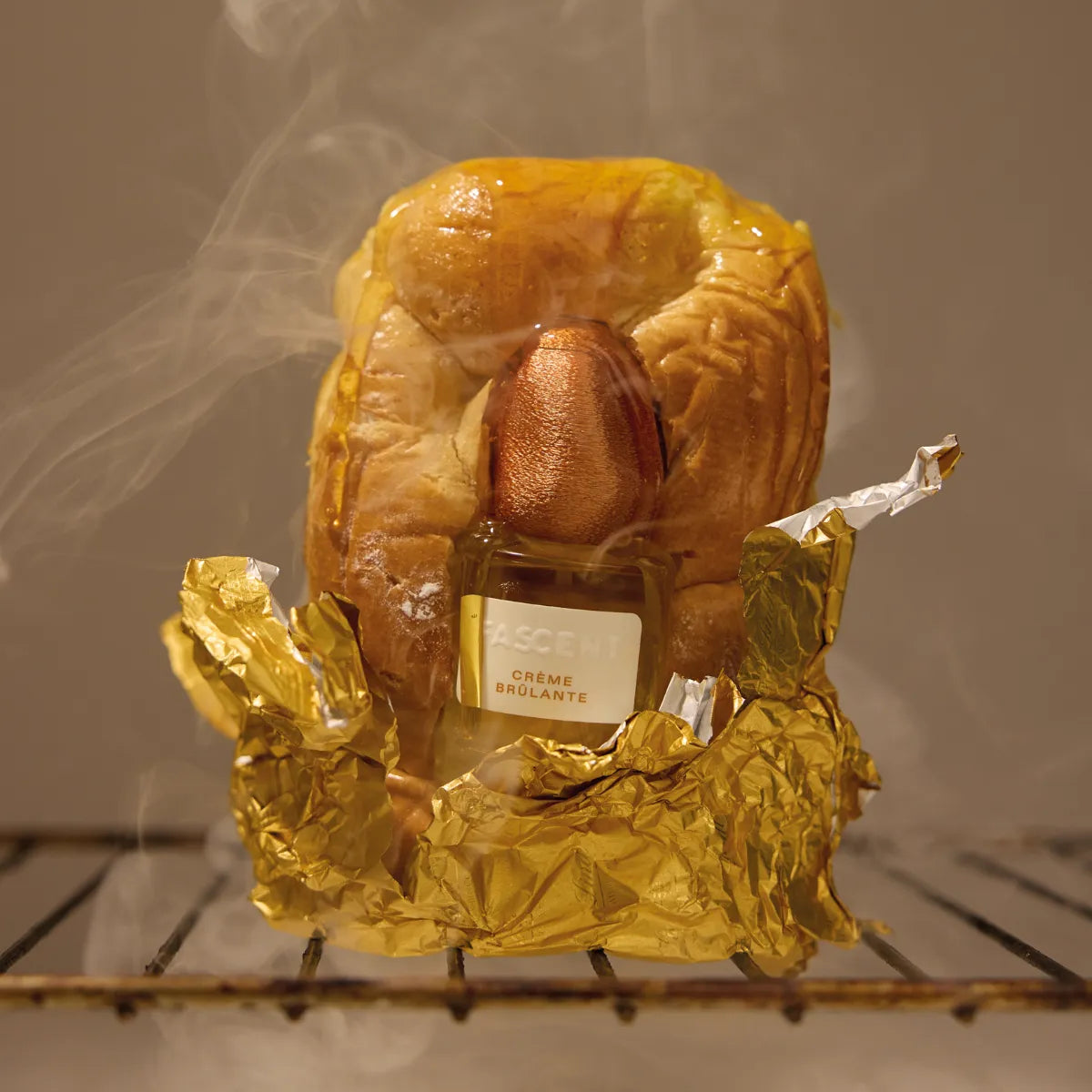 Fascent - Crème Brûlante Parfumflakon umhüllt von goldener Folie vor dampfigem, warmem Hintergrund