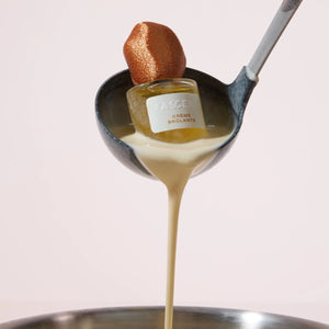 Fascent - Crème Brûlante Parfumflakon präsentiert in Kelle mit cremigem, vanillig-holzigem Aroma vor hellem Hintergrund