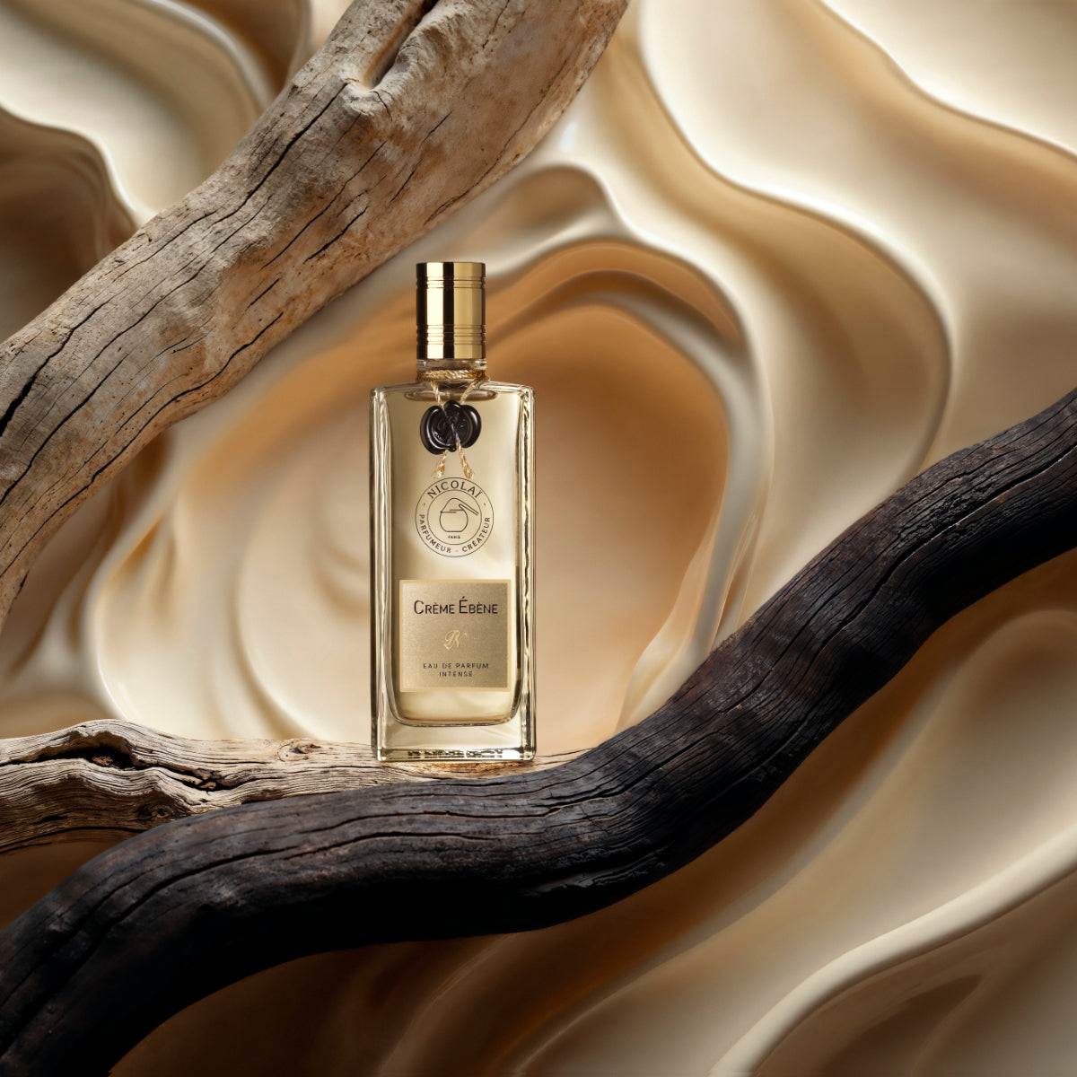 Nicolaï - Crème Ébène Intense EdP Flakon mit goldenem Verschluss vor seidig-beiger Hintergrundgestaltung und Holzdekoration