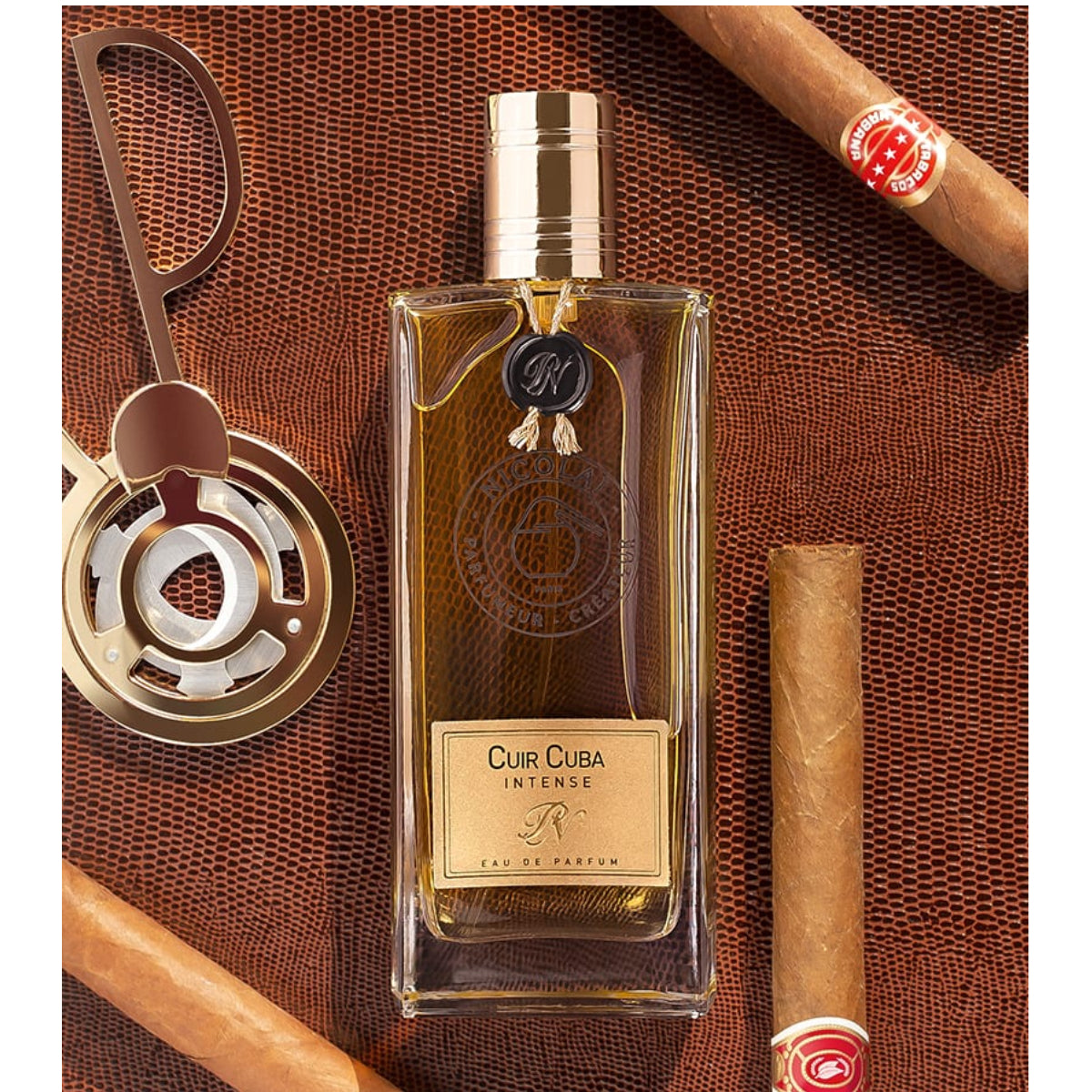 Nicolaï - Cuir Cuba Intense Parfümflakon mit goldfarbenem Verschluss auf Lederhintergrund mit Zigarren und Humidorzubehör