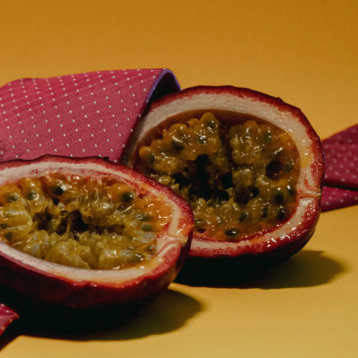 Sous Le Manteau - Cuir D'Orient mit reifer Passionsfruchthälfte auf gelbem Hintergrund und rotem Stoff