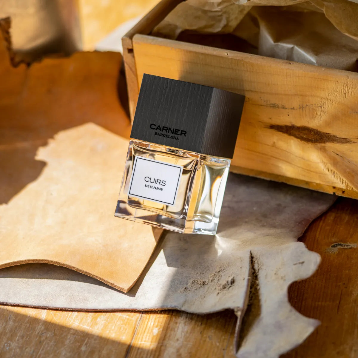 Carner Barcelona - Cuirs Parfumflakon mit klaren Linien und dunklem Holzdeckel auf Lederstücken und Holzplatte