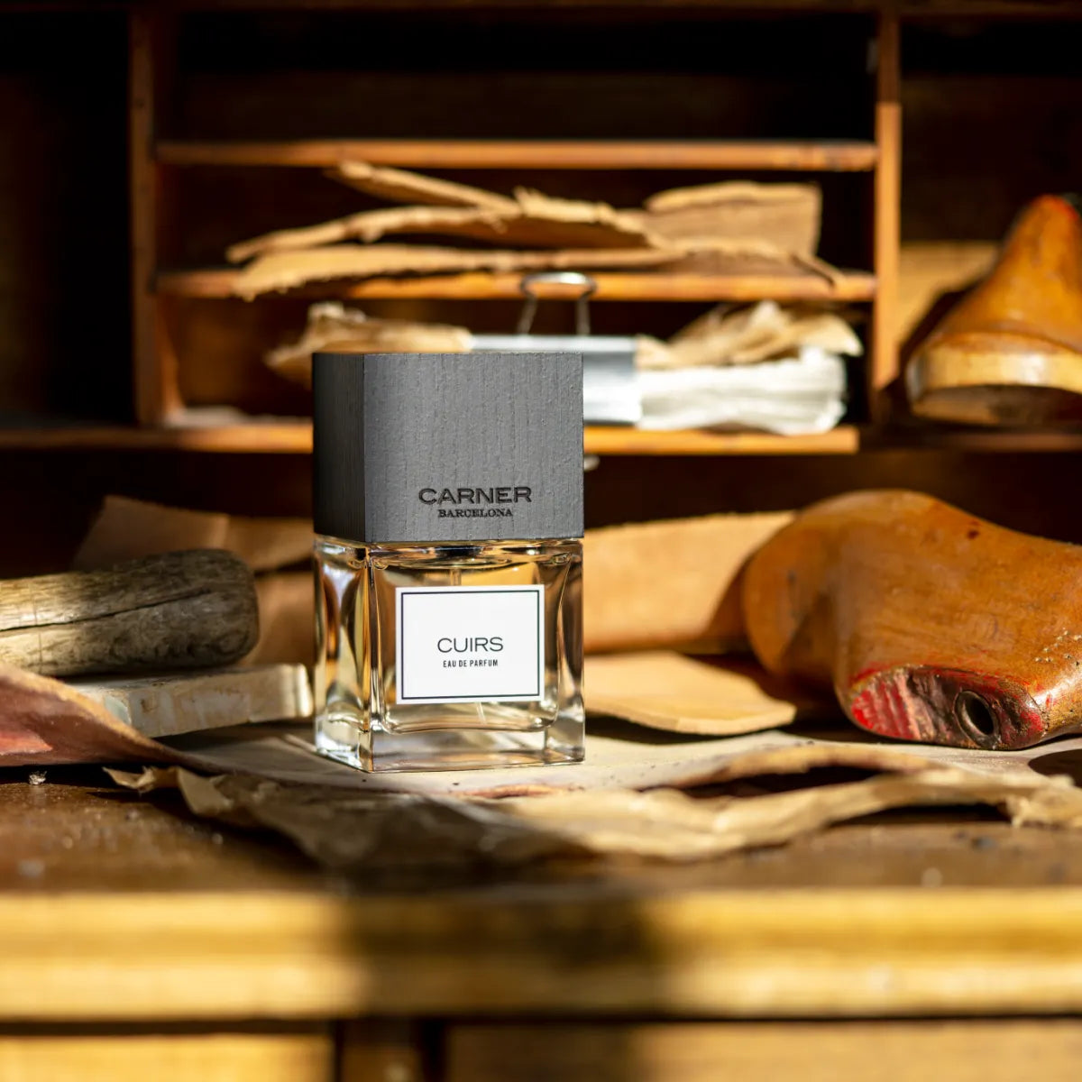 Carner Barcelona - Cuirs Parfumflakon mit mattschwarzem Verschluss auf Vintage-Lederwerkstatt-Hintergrund