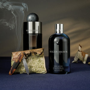 Molton Brown - Dark Leather Bath & Shower Gel in dunkler Flasche mit silbernem Verschluss vor edlem Hintergrund