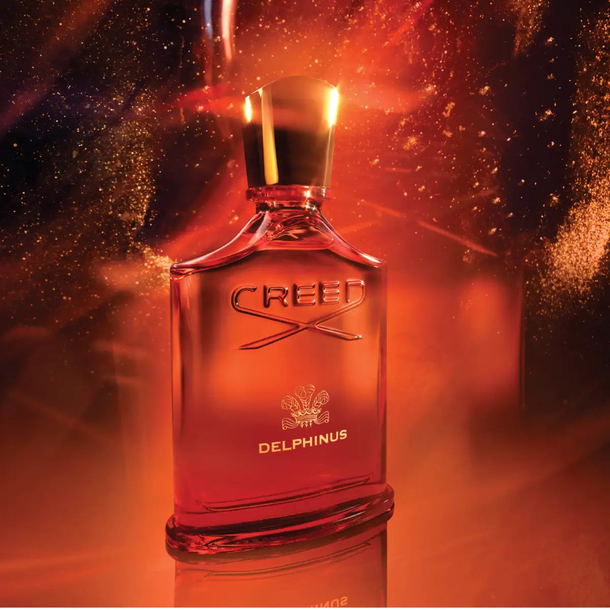 Creed - Delphinus Parfümflakon in leuchtendem Orange mit goldenem Verschluss und funkelndem Amber-Effekt im Hintergrund